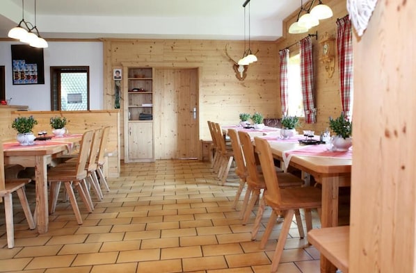 A wooden interior with multiple dining tables and chairs, a herringbone floor pattern, and pendant lighting.
