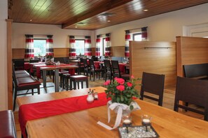 A restaurant with wooden tables and benches, red table runners, and striped curtains. - Gasthof Alpe (Philippsreut)