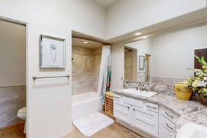 Un baño moderno con bañera, lavamanos con encimera de mármol y un espejo grande.