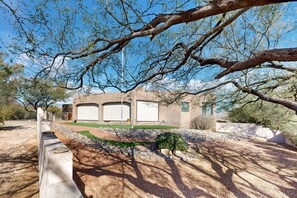 Una casa con garaje, un jardín ajardinado con un pequeño árbol y un muro de piedra.
