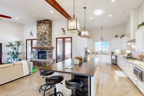 A spacious kitchen with a central island, white cabinetry, and a stone fireplace.