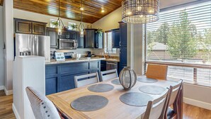 Una cocina moderna con armarios oscuros, electrodomésticos de acero inoxidable y una mesa de comedor de madera con cuatro sillas.