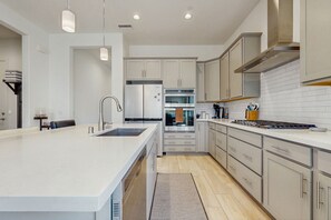 A modern kitchen with a large island, stainless steel appliances, and light-colored cabinetry. - Bright desert oasis  w/hot tub & grill - shared pool & tennis in  55+ community (Rancho Mirage)