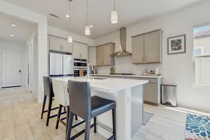 A modern kitchen with a central island, stainless steel appliances, and pendant lighting. - Bright desert oasis  w/hot tub & grill - shared pool & tennis in  55+ community (Rancho Mirage)
