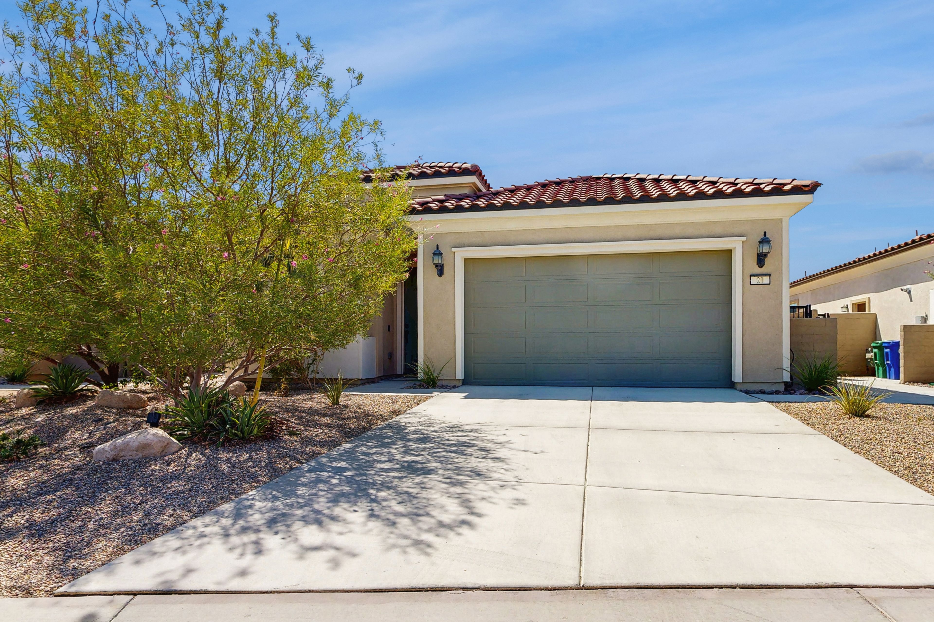 A residential house with a garage, a driveway, and a landscaped garden with rocks and a tree.