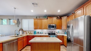 A modern kitchen with wooden cabinets, stainless steel appliances, and a central island. - Spacious home surrounded by palms with pool, grill, children (Litchfield Park)