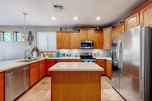 A modern kitchen with wooden cabinets, stainless steel appliances, and a central island. - Spacious home surrounded by palms with pool, grill, children (Litchfield Park)