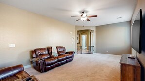 A living room with a brown leather sofa, a brown leather recliner, a ceiling fan, and a flat-screen TV mounted on the wall. - Spacious home surrounded by palms with pool, grill, children (Litchfield Park)
