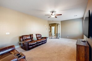 A living room with a brown leather sofa, a brown leather recliner, a ceiling fan, and a flat-screen TV mounted on the wall. - Spacious home surrounded by palms with pool, grill, children (Litchfield Park)