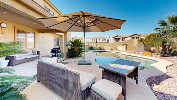 A patio area with wicker furniture, a table, and an umbrella. - Spacious home surrounded by palms with pool, grill, children (Litchfield Park)