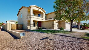A two-story house with a balcony, a driveway, and a tree in front. - Spacious home surrounded by palms with pool, grill, children (Litchfield Park)