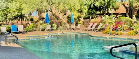 A swimming pool with lounge chairs and umbrellas, surrounded by trees and a fence.