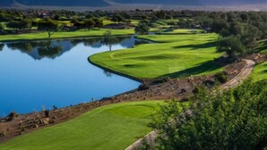 Een golfbaan met een vijver, bomen en bergen op de achtergrond.