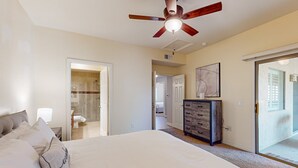 Een slaapkamer met een groot bed, een plafondventilator, een dressoir en een glazen schuifdeur naar een balkon.