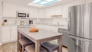 A modern kitchen with white cabinets, a stainless steel refrigerator, a microwave, and a large island with stools. - Dog-friendly mountain-view home with private pool, outdoor lounging & W/D (Cave Creek)