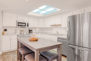 A modern kitchen with white cabinets, a stainless steel refrigerator, a microwave, and a large island with stools. - Dog-friendly mountain-view home with private pool, outdoor lounging & W/D (Cave Creek)