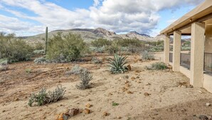 A desert landscape with sparse vegetation, a building with a beige exterior, and distant mountains under a partly cloudy sky. - Dog-friendly mountain-view home with private pool, outdoor lounging & W/D (Cave Creek)