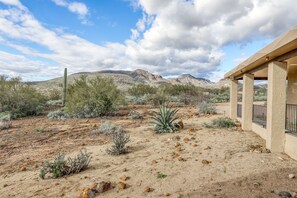 A desert landscape with sparse vegetation, a building with a beige exterior, and distant mountains under a partly cloudy sky. - Dog-friendly mountain-view home with private pool, outdoor lounging & W/D (Cave Creek)