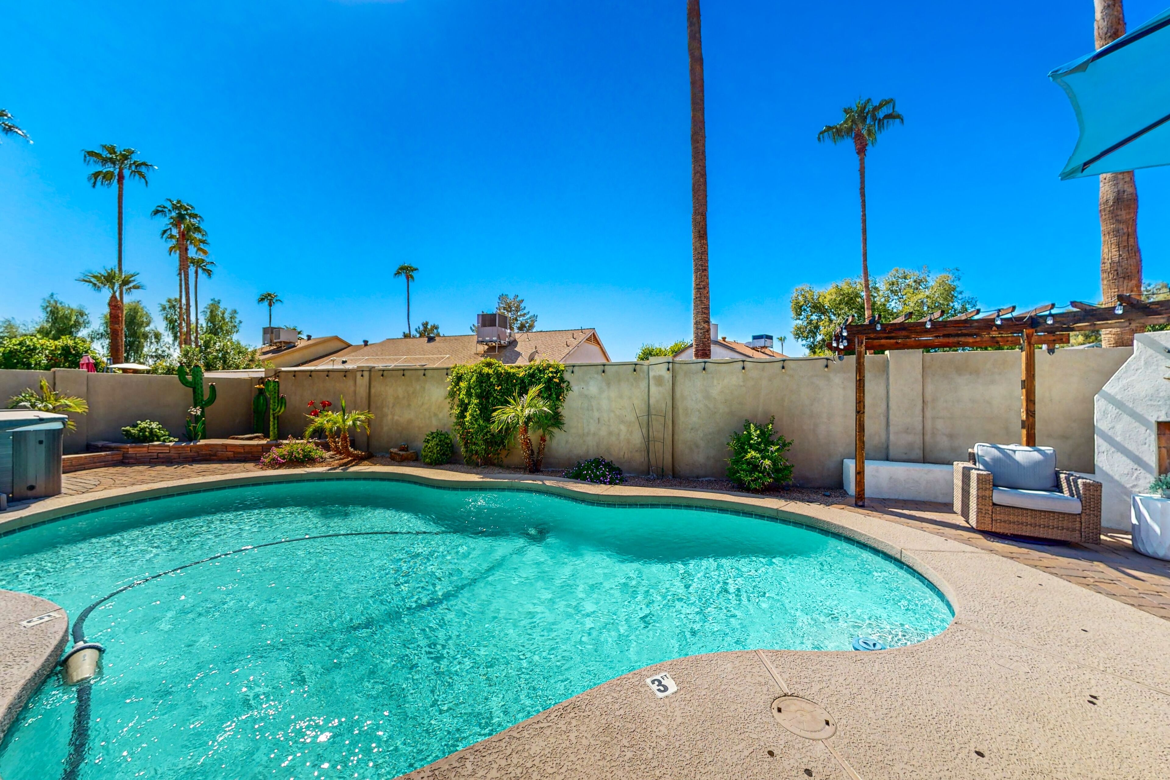 A swimming pool with a curved edge, surrounded by a concrete deck and a pergola with lights.
