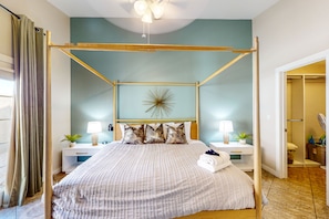 Een slaapkamer met een hemelbed, nachtkastjes met lampen, een decoratief wandobject en uitzicht op de badkamer.