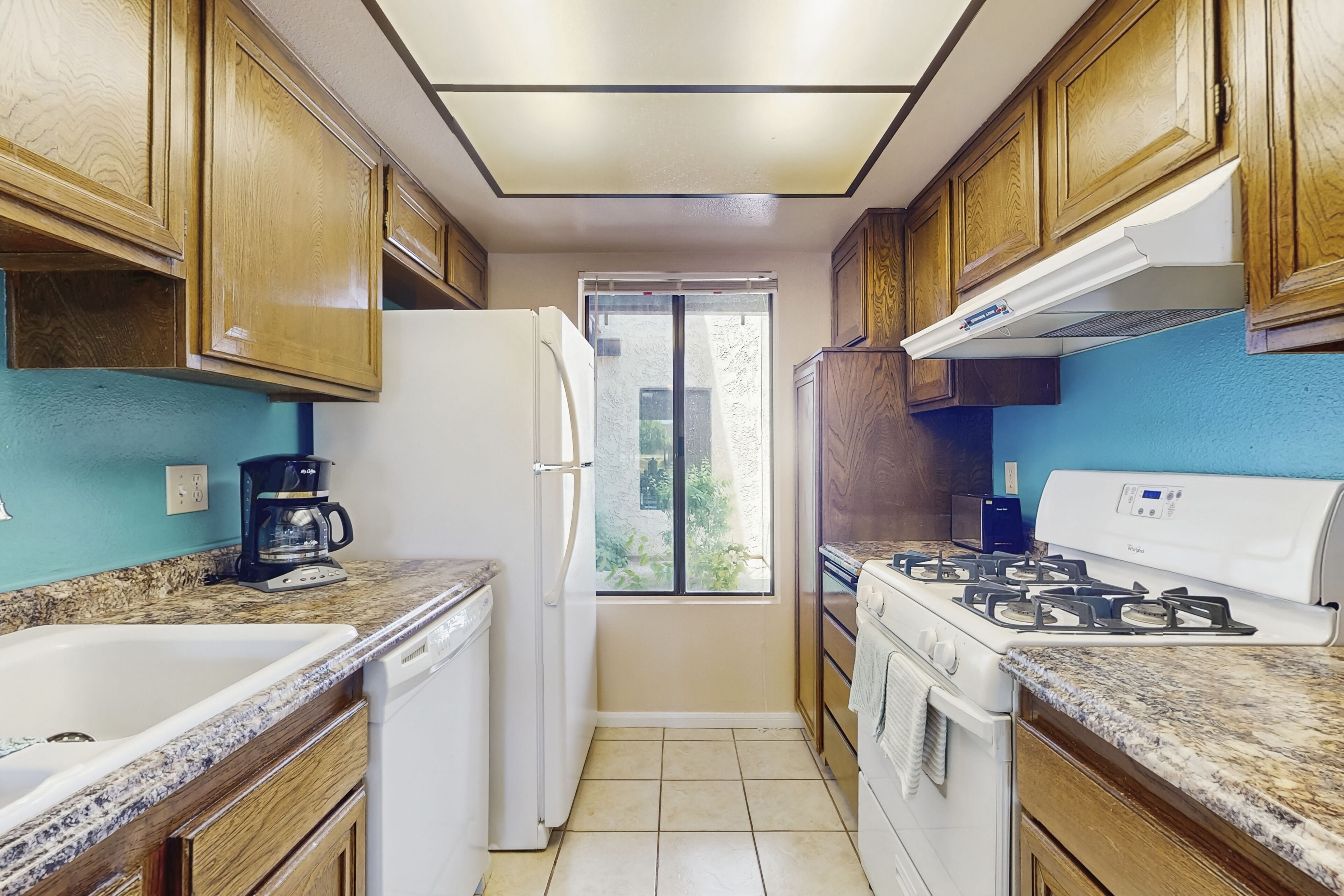 Una cocina compacta con armarios de madera, un refrigerador blanco, una estufa y una cafetera.