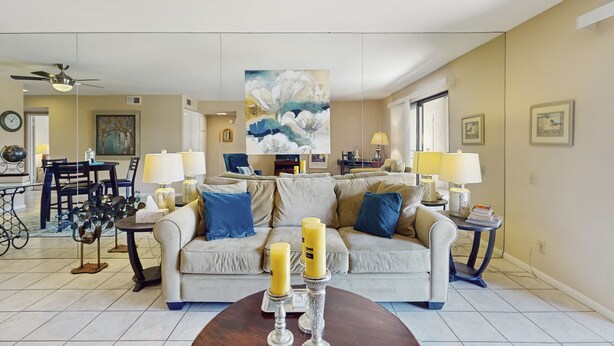 Ein Wohnzimmer mit einem beigefarbenen Sofa, zwei blauen Kissen, einem Couchtisch mit Kerzen und einem Gemälde über dem Sofa.