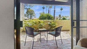 Eine Terrasse mit zwei Stühlen und einem Tisch, Blick auf Palmen und einen klaren Himmel.