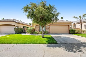 A residential street with two houses, each with a garage, a well-maintained lawn, and a tree in the center. - Elegant dog-friendly home on the golf course with private pool & spa (Cathedral City)
