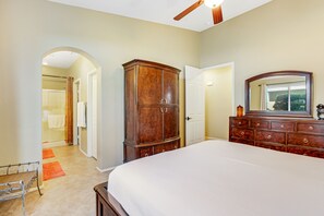 A bedroom with a large bed, wooden dresser, and a mirror. There is a door leading to a bathroom with a shower and a towel rack. - Elegant dog-friendly home on the golf course with private pool & spa (Cathedral City)
