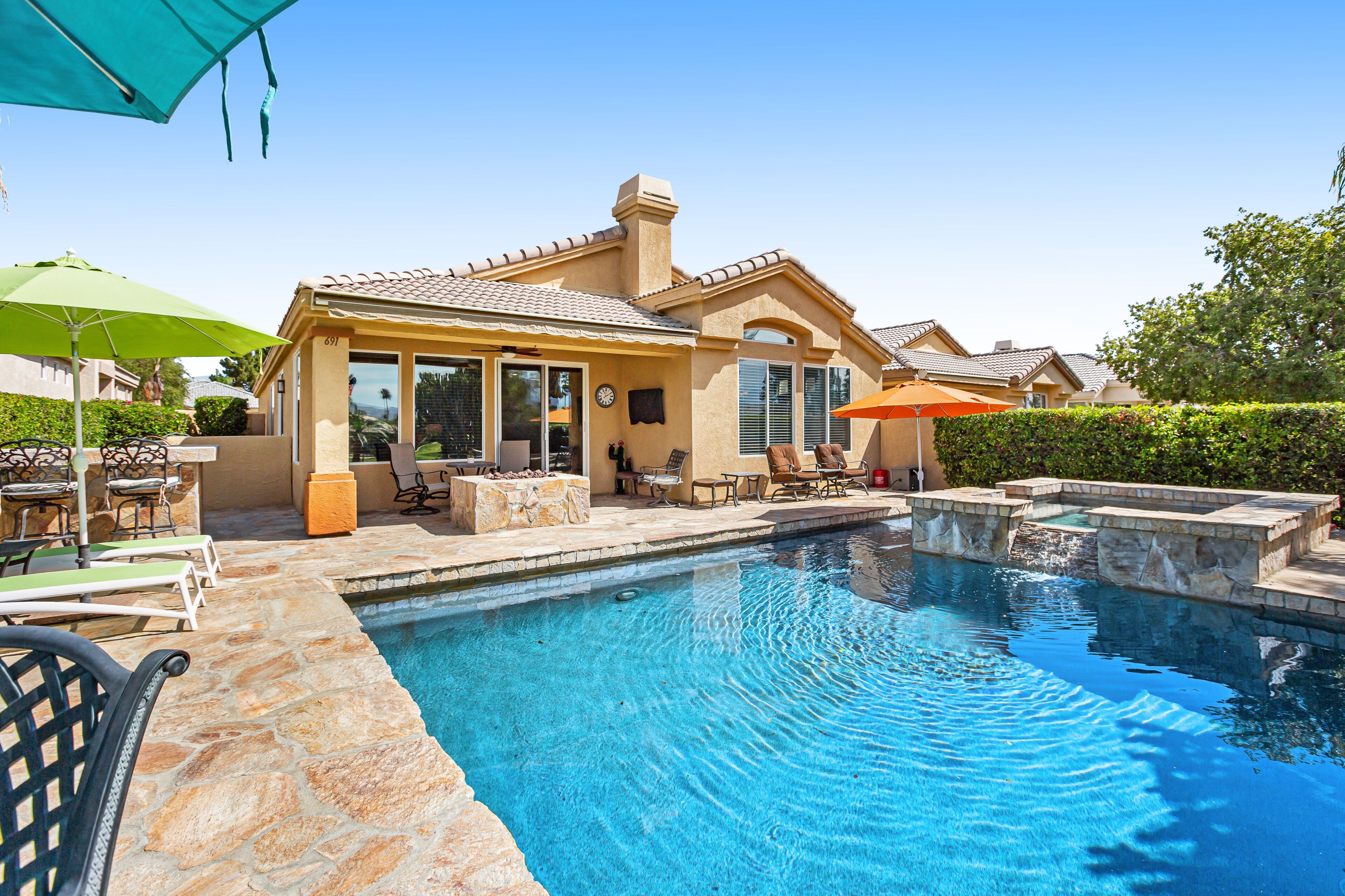 A residential property with a swimming pool, outdoor seating, and a covered patio area.