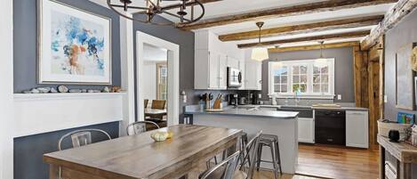 A modern kitchen with a central island, wooden dining table, and bar stools.