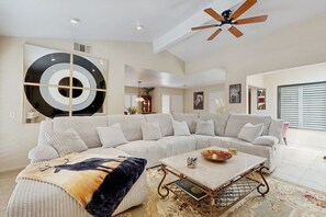 Ein geräumiges Wohnzimmer mit Ecksofa, Couchtisch und Deckenventilator.