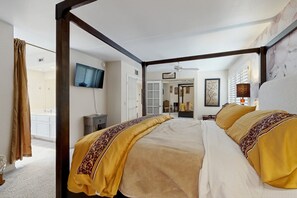 Ein Bett mit Baldachin, ein an der Wand befestigter Fernseher und eine Tür zu einem Badezimmer.