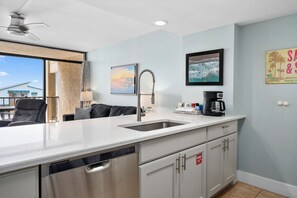 A modern kitchen with a large island, a built-in dishwasher, and a coffee station. - Windward 312 at Laguna Reef - Bay Views (Rockport)