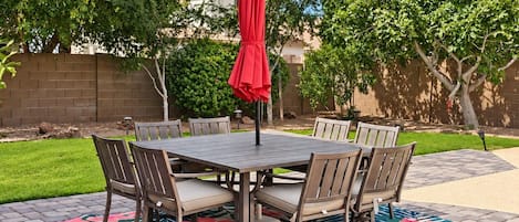 An outdoor patio with a round table and chairs, a red umbrella, and a patterned rug.