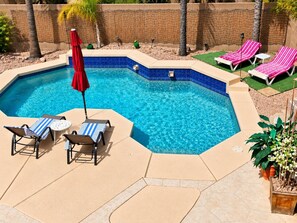 A swimming pool with a blue tiled edge, surrounded by beige tiles and a small patio area with lounge chairs and a red umbrella. - Beautiful home with private pool, W/D, central AC & great locale - dog-friendly (Mesa)