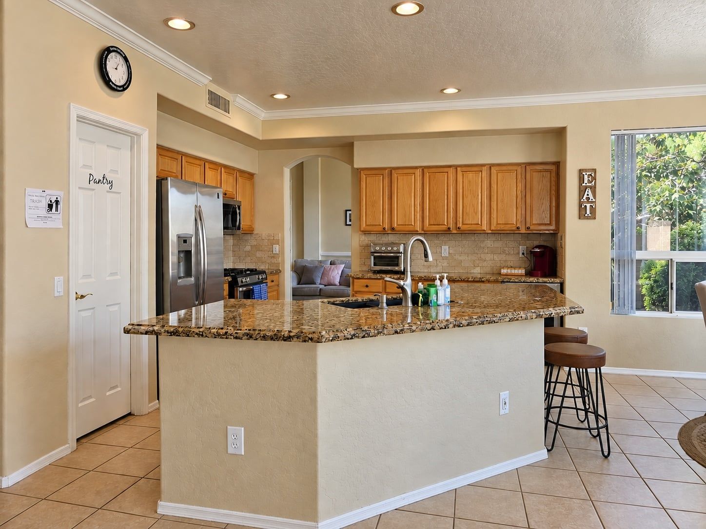 A kitchen with a central island, wooden cabinets, a stainless steel refrigerator, and a clock on the wall.