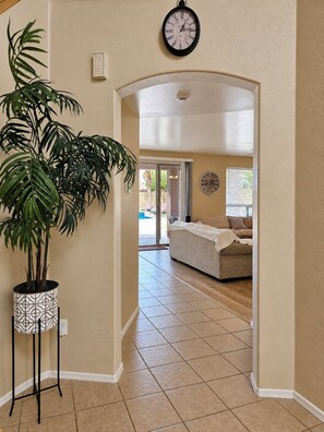 A hallway with a potted plant, a clock, and a living room in the background. - Beautiful home with private pool, W/D, central AC & great locale - dog-friendly (Mesa)