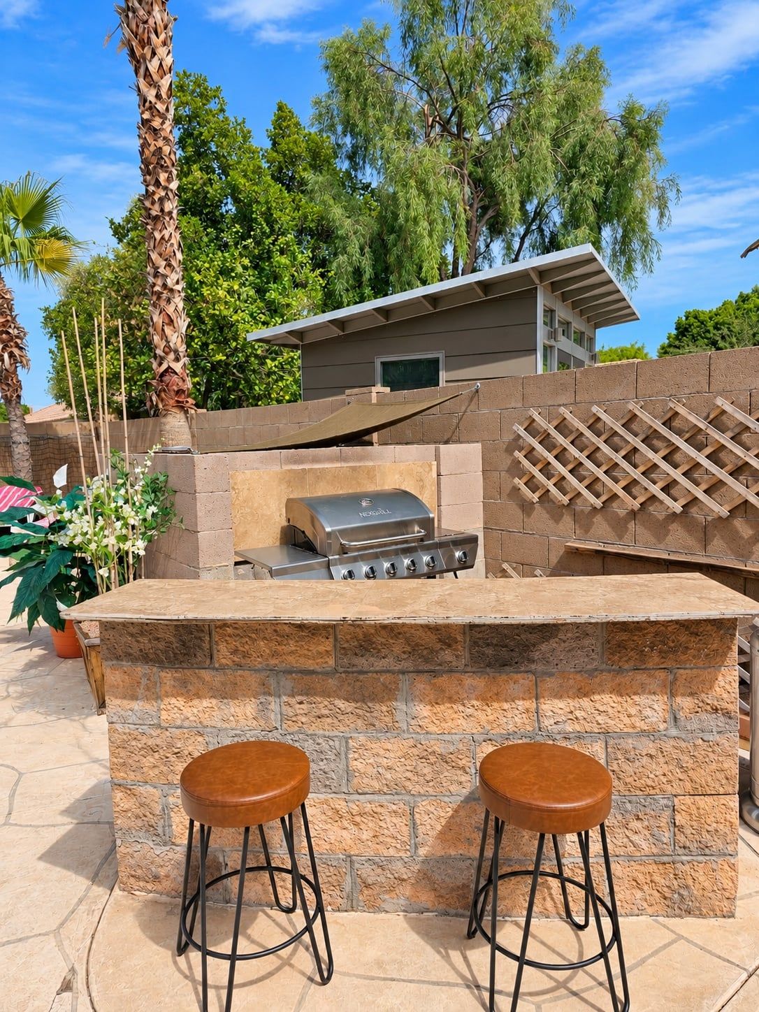 An outdoor bar area with a stone countertop, two stools, and a grill.