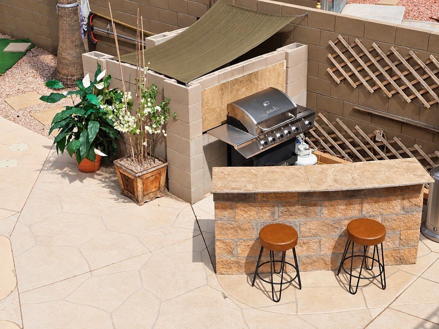 An outdoor barbecue area with a built-in grill, two stools, and potted plants.