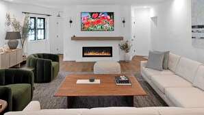 Un salon moderne avec une cheminée, des canapés verts et beiges, une table basse et un tableau au-dessus de la cheminée.