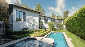 Une maison moderne dotée d’une piscine, entourée de haies et d’arbres bien entretenus.