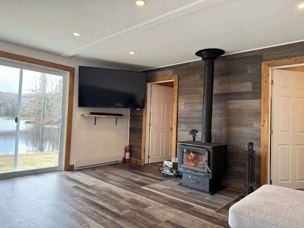 A modern living room with a fireplace, a flat-screen TV, and a large window overlooking a lake.