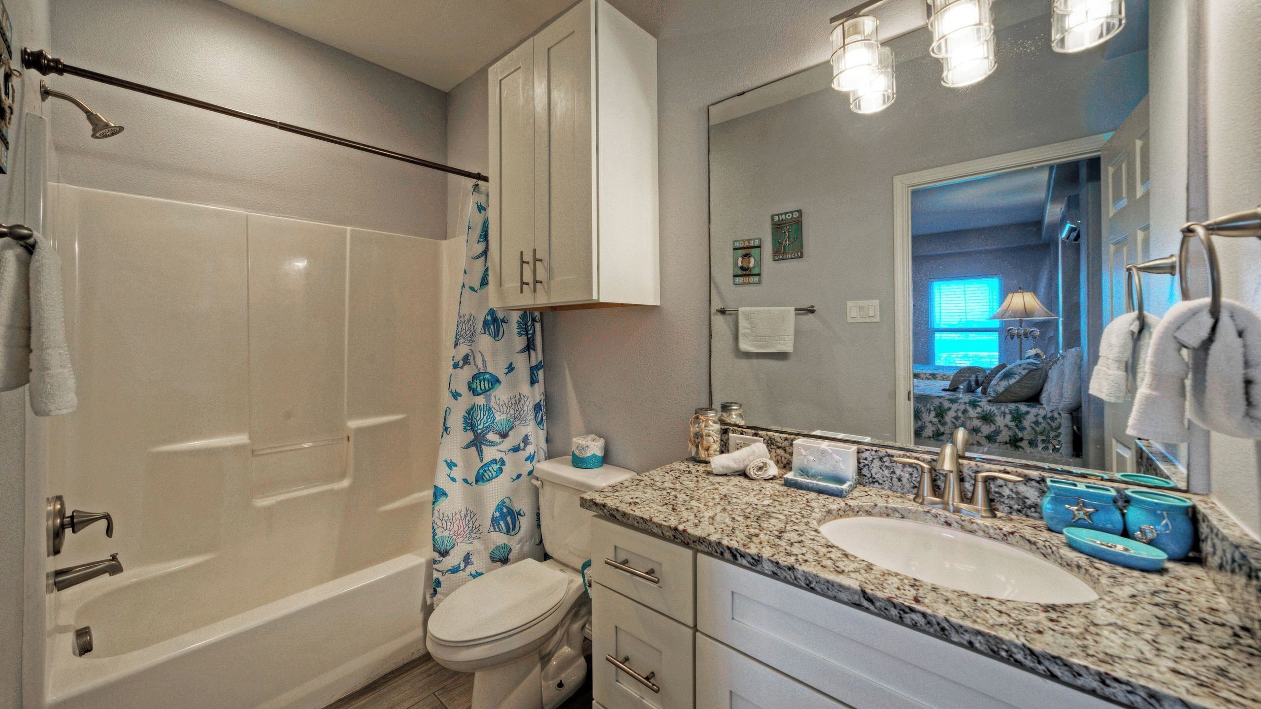 A bathroom with a bathtub, toilet, vanity with a sink, and a shower curtain with a marine design.