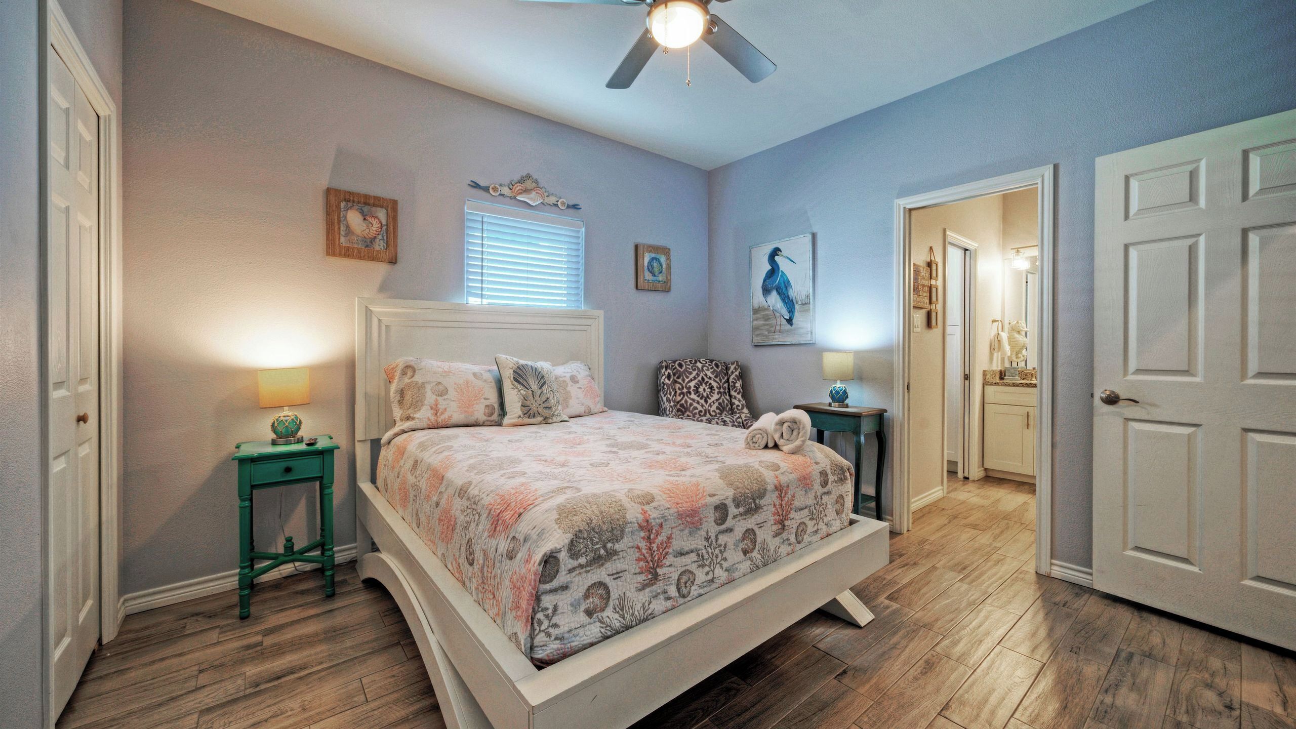 A bedroom with a bed, two nightstands, a ceiling fan, and a door leading to another room.