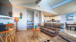 A modern living room with a leather sofa, wooden coffee table, and a kitchen in the background. - La Sirena by Avantstay Communal Pool + Covered Lounge + Marsh Views + Near Port A Beach (Port Aransas)