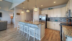 A modern kitchen with a central island, bar stools, stainless steel appliances, and a tiled backsplash. - La Sirena by Avantstay Communal Pool + Covered Lounge + Marsh Views + Near Port A Beach (Port Aransas)