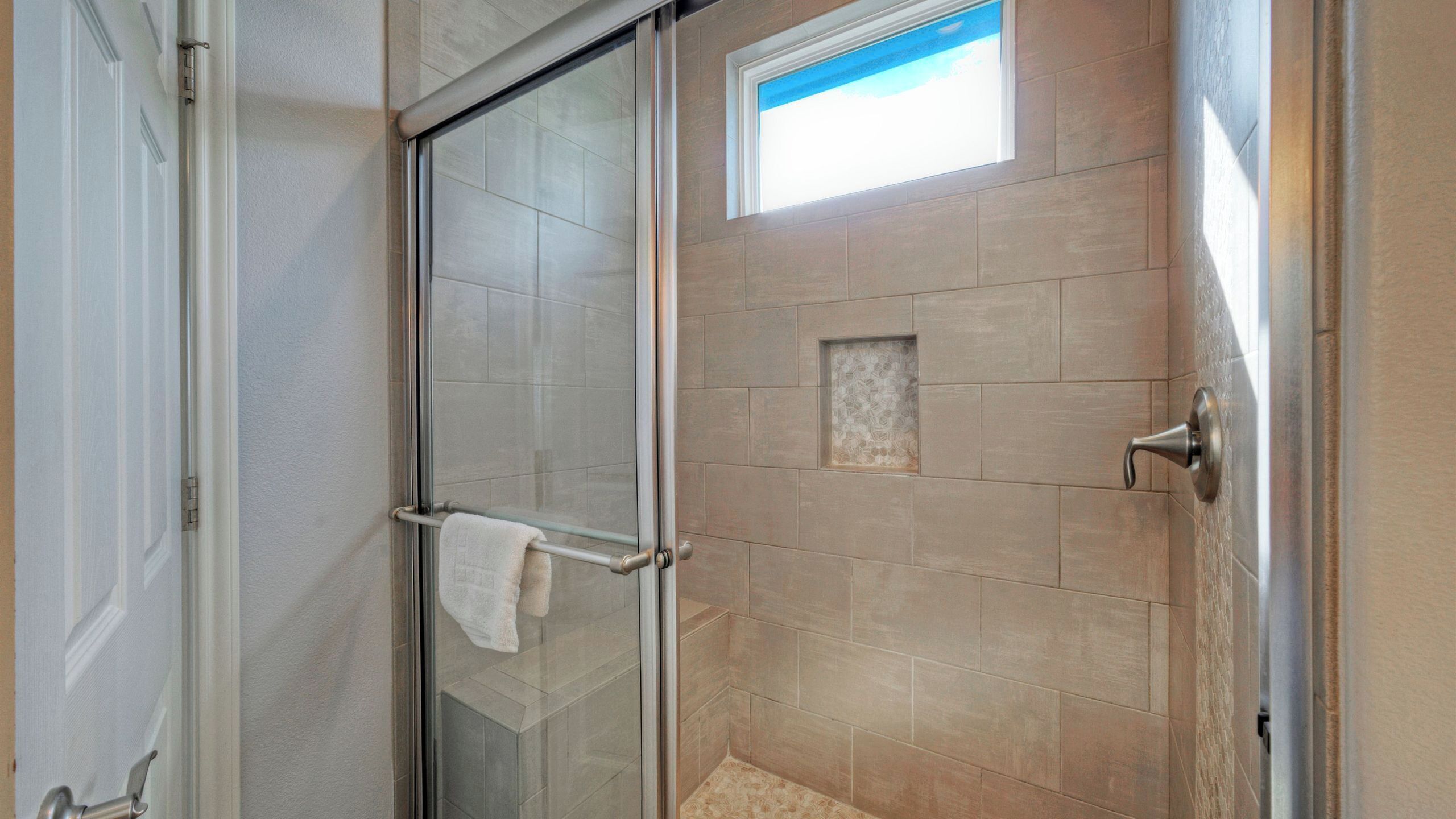 Ducha con cerramiento de vidrio, un perchero, una ventana pequeña y pared de azulejos.