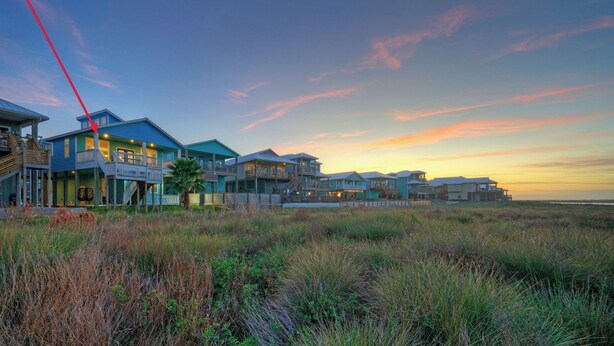 A coastal property with multiple buildings, a prominent red beam, and a sunset view. - La Sirena by Avantstay Communal Pool + Covered Lounge + Marsh Views + Near Port A Beach (Port Aransas)