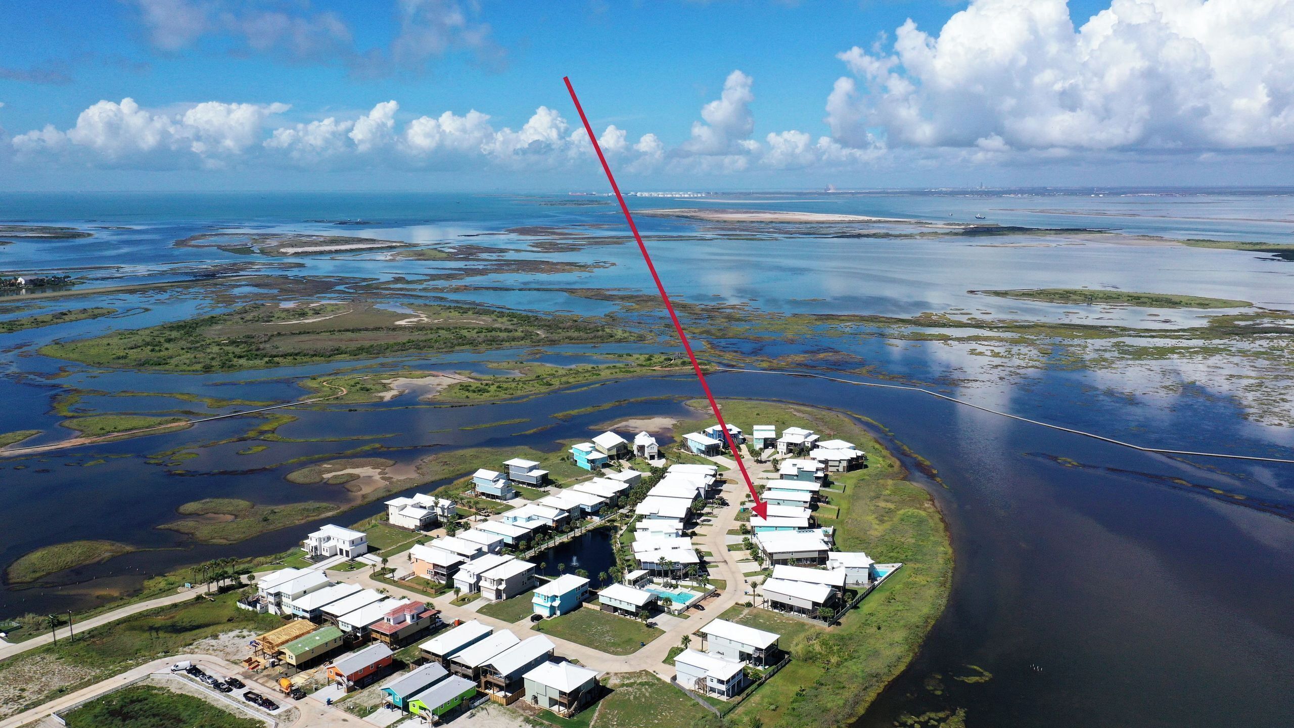 Vue aérienne d’une zone résidentielle côtière, avec des maisons, un port de plaisance et une ligne rouge indiquant un chemin ou une limite.